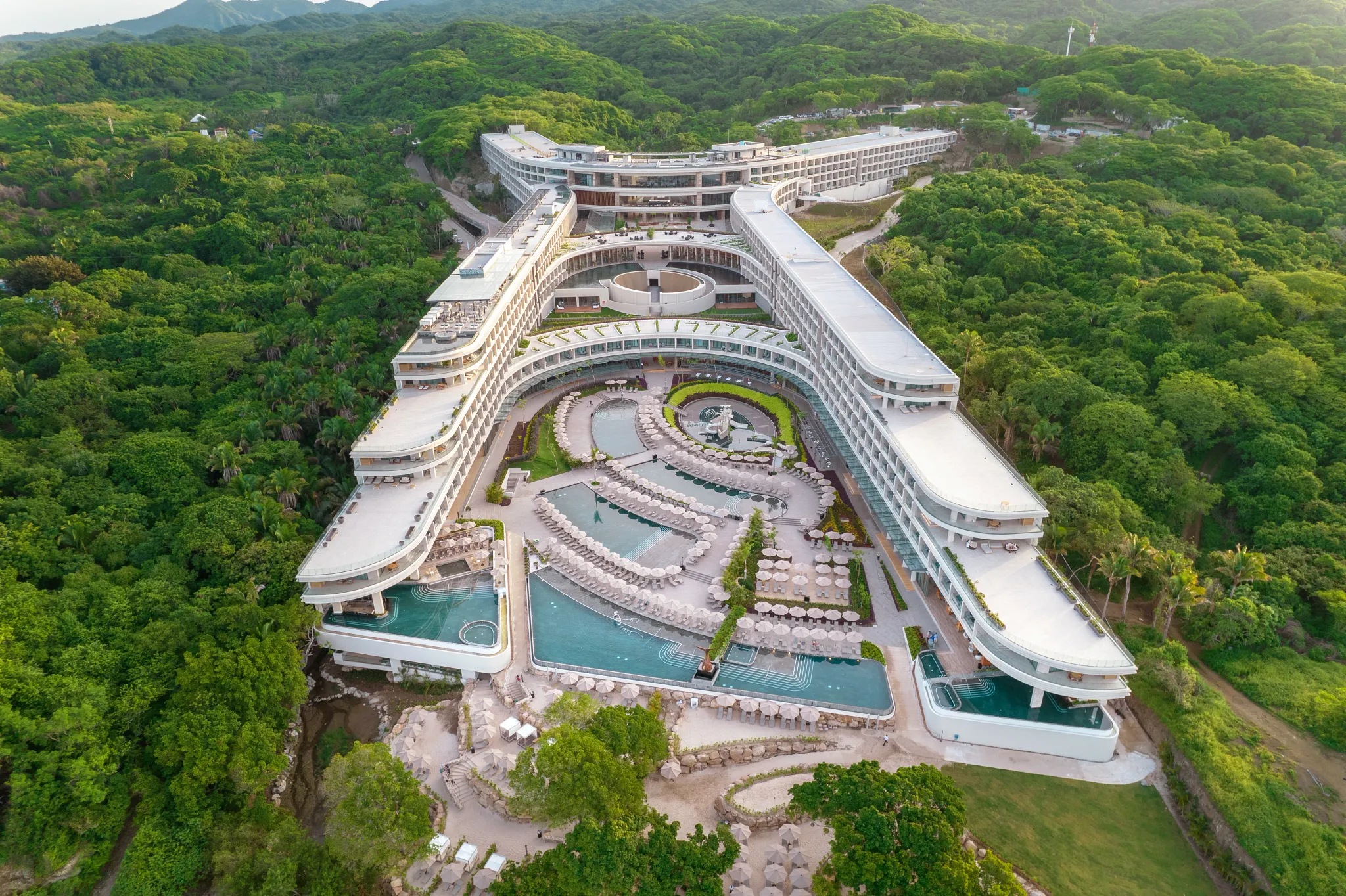 Aerial view of infinity pools and modern architecture at Secrets Bahia Mita Surf & Spa Resort surrounded by lush jungle.