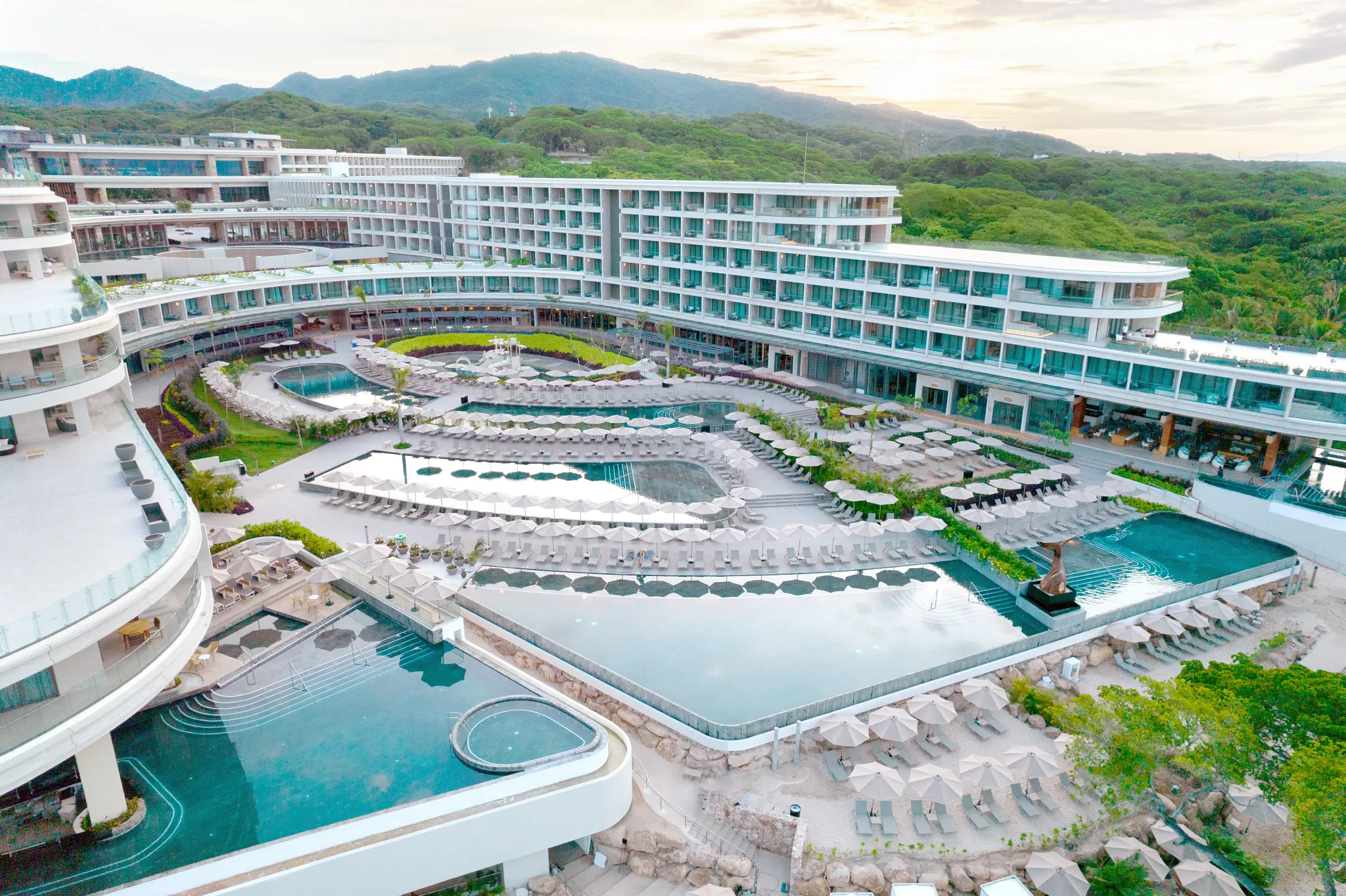 Aerial view of multiple swimming pools and sun loungers at Secrets Bahia Mita Surf & Spa Resort overlooking the Pacific Ocean.
