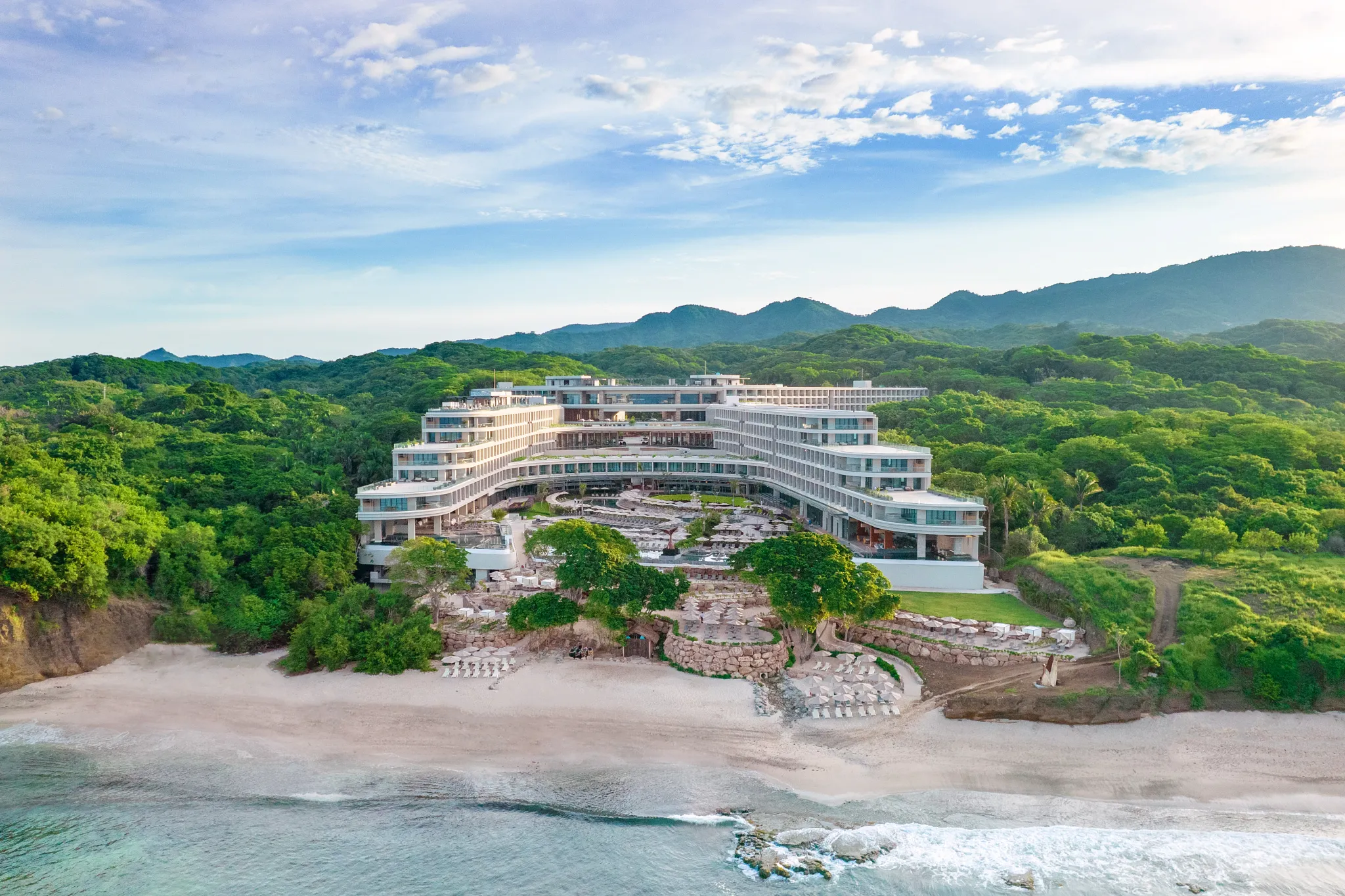 Aerial view of Secrets Bahia Mita Surf & Spa Resort nestled between lush jungle and the Pacific Ocean in Riviera Nayarit.