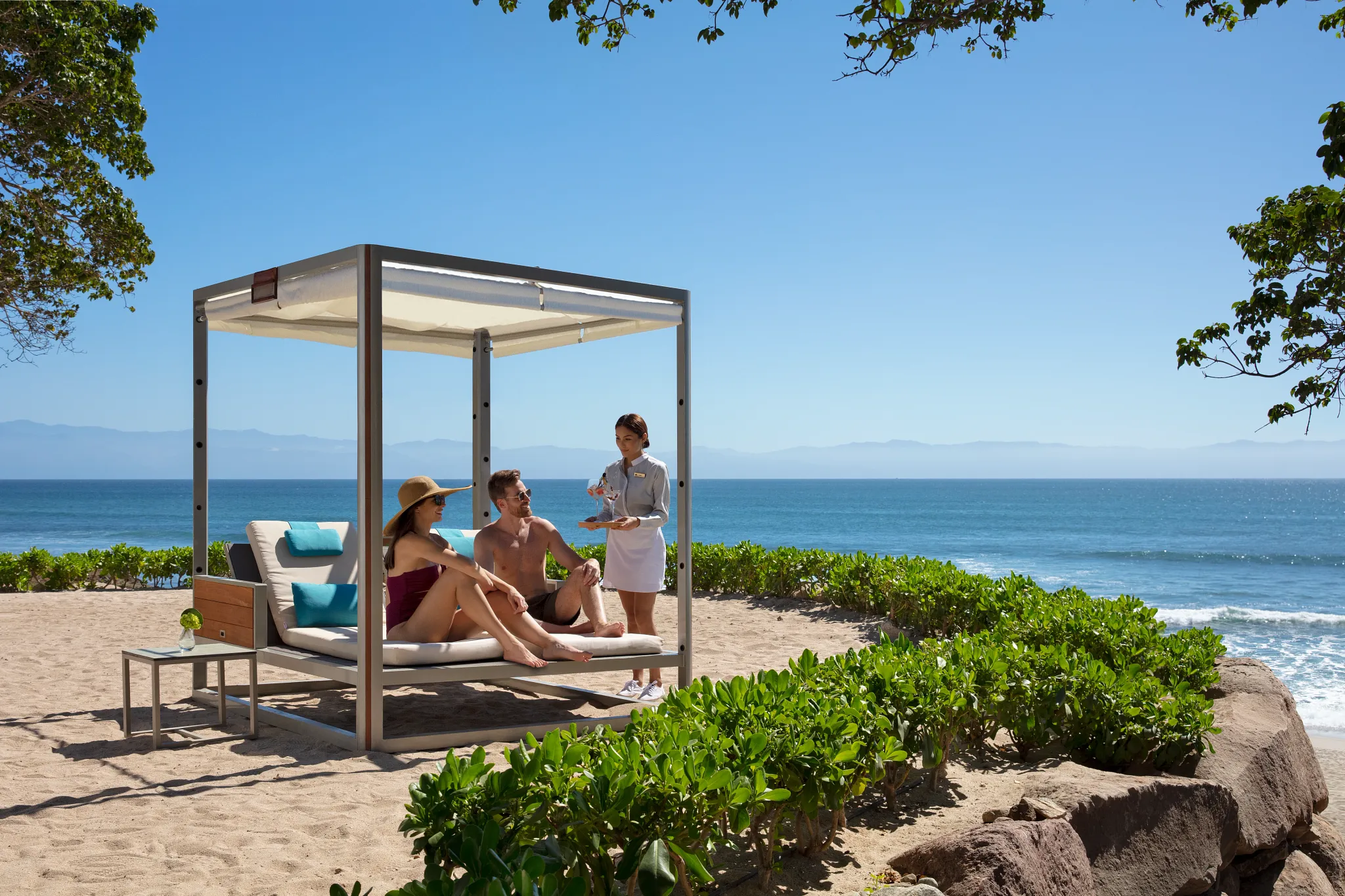 Guest relaxing on a beach cabana with wait service at Secrets Bahia Mita Surf & Spa Resort overlooking the Pacific Ocean.