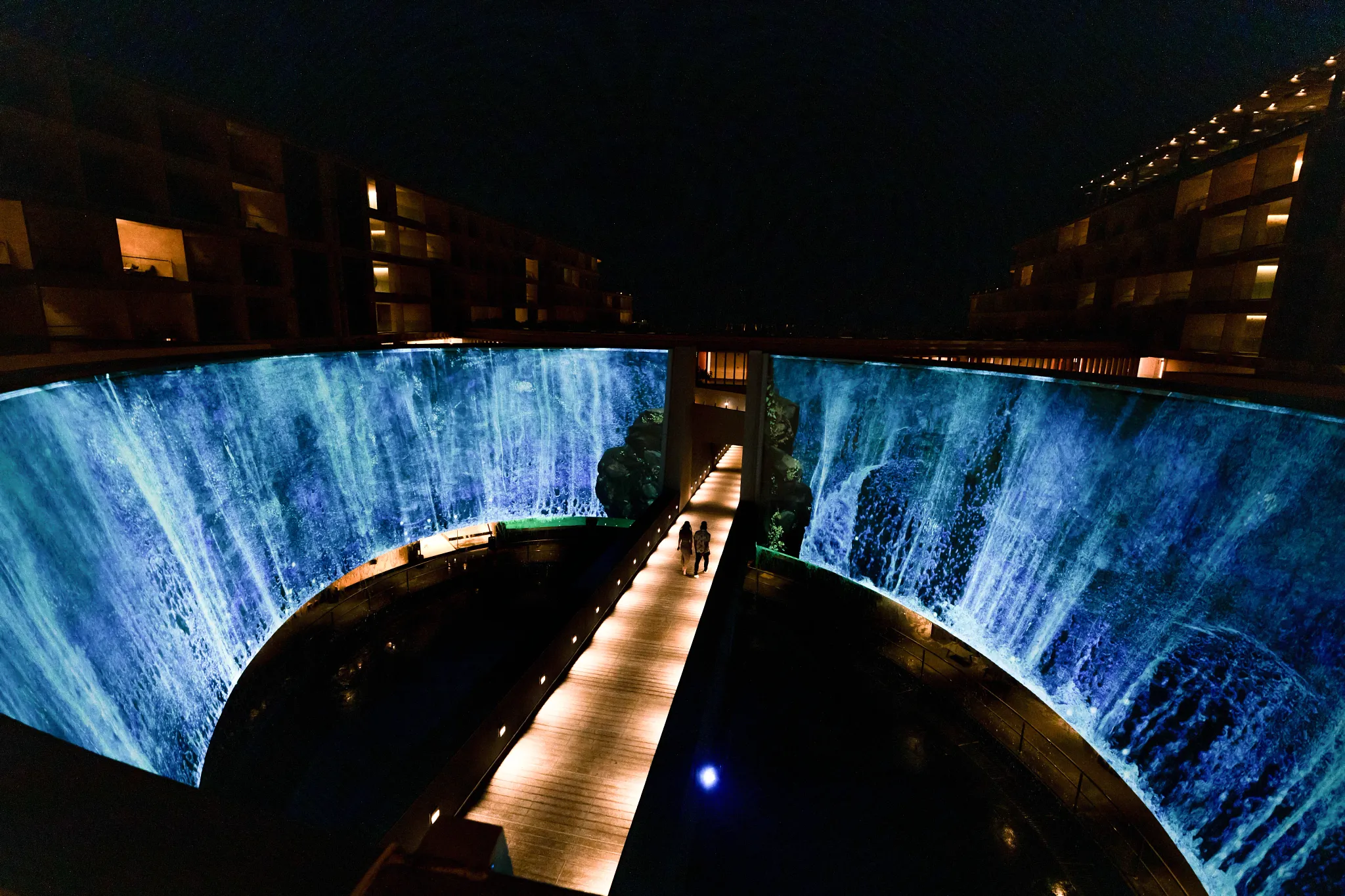Illuminated immersive art wall and walkway at night inside Secrets Bahia Mita Surf & Spa Resort.