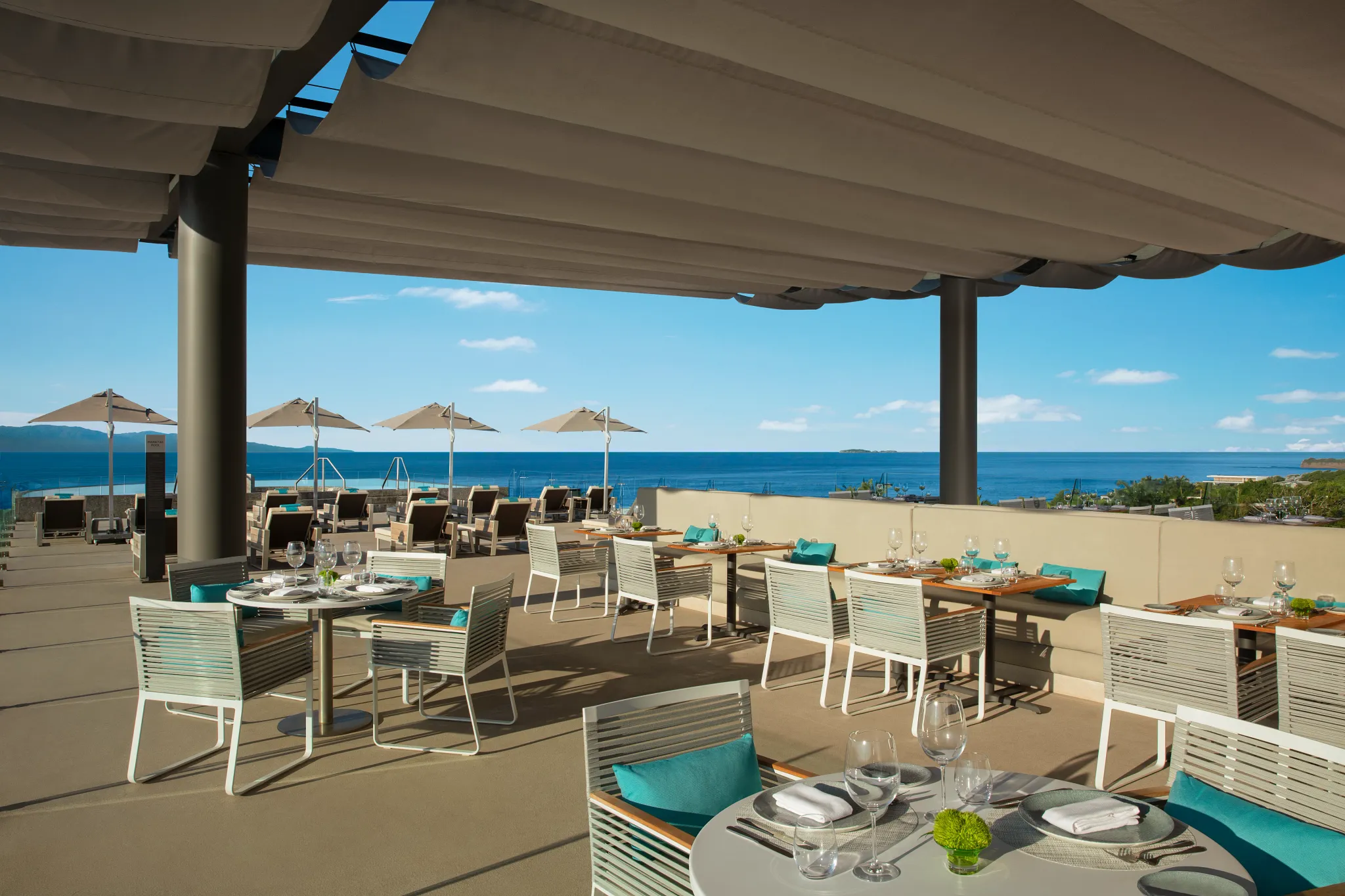 Olio Mediterranean and Seafood Restaurant at Secrets Bahia Mita Surf & Spa Resort featuring open-air oceanview dining with modern tables and coastal décor.